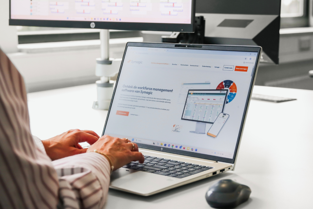 Close-up van iemand die werkt op een laptop met de website van Symagic open, waarop workforce management-software wordt getoond. De afbeelding benadrukt technologie en efficiënt plannen.